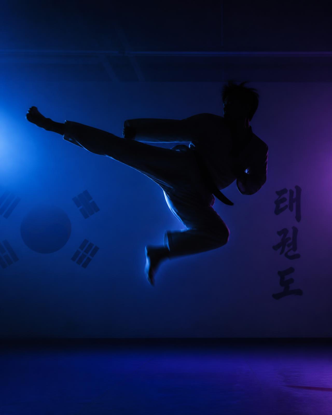 Taekwondo athlete executing a mid-air kick under stage lighting